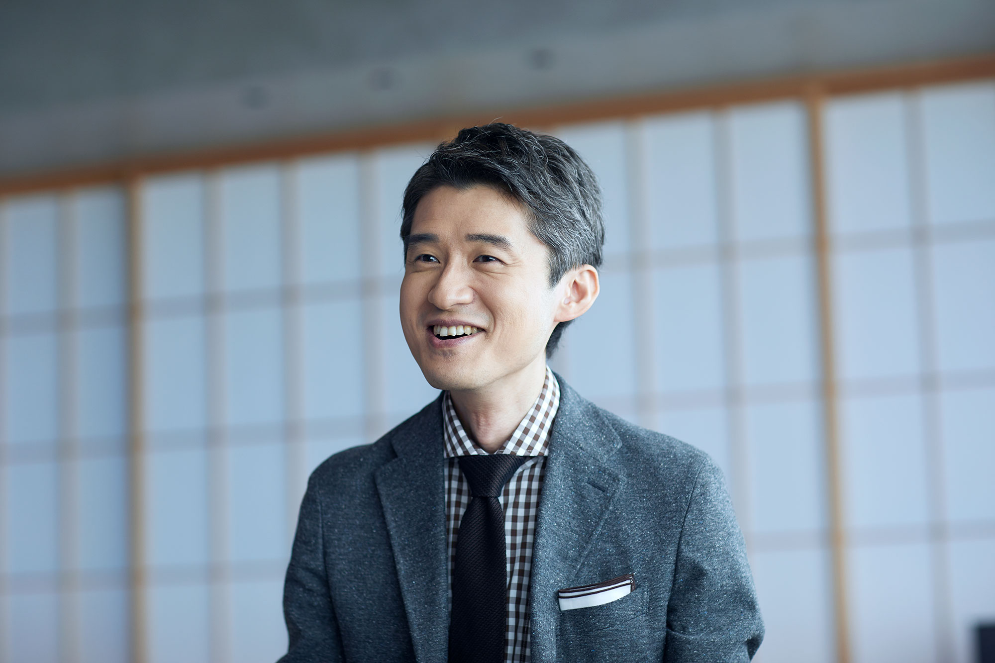 Hishashi Fujieda in a grey suit, gingham shirt, and black tie.