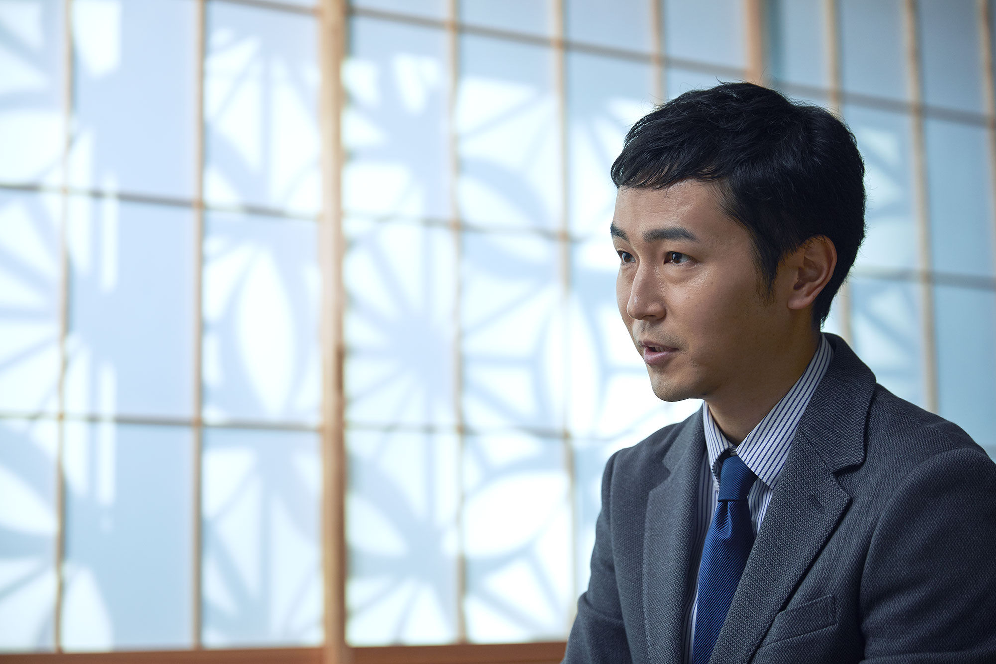 Kiyotaka Sakai wearing a grey suit and striped shirt with tie.